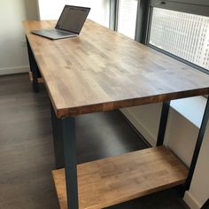 a wooden table with a laptop on top of it next to a window in an office