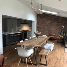 a dining room table with white chairs and wooden benches in front of an open kitchen