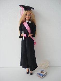 a barbie doll wearing a graduation gown and holding a pink sash next to a stack of books