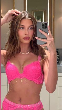 a woman taking a selfie in a pink bra top and panties with her cell phone