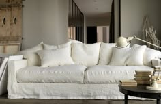 a white couch sitting next to a wooden table with books on it and a lamp in the corner