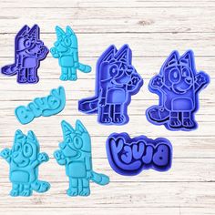 five cookie cutters with cartoon characters in blue and purple on wooden background, one is shaped like an elephant