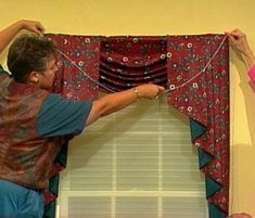 two people are hanging up the curtains in front of a window with their hands on them