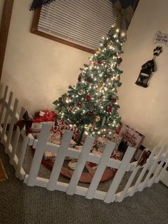 a small christmas tree in a room with white picket fence and presents on the floor