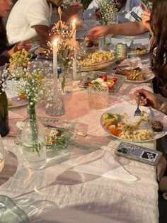 a group of people sitting around a table with plates of food and candles on it