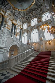 an ornate staircase with red carpet and white railings in a large palace like building