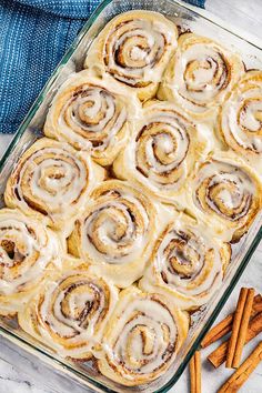 cinnamon rolls in a casserole dish with cinnamon sticks next to it on a table