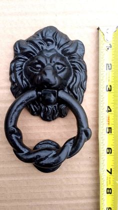 a black lion head door knocker next to a ruler