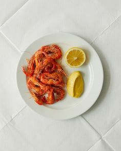 a white plate topped with cooked shrimp next to a lemon wedge on top of a table