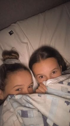 two girls wrapped up in blankets on a bed