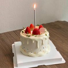 a white cake with strawberries on top sitting on a table next to a lit candle