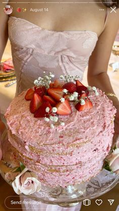 a woman holding a pink cake with strawberries on top and flowers in the middle