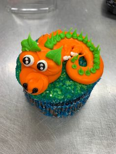 a cupcake decorated with an orange and green dragon on it's side, sitting on a silver surface