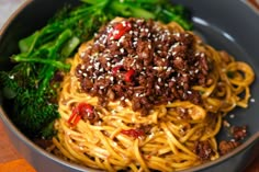 a bowl filled with noodles and vegetables on top of a wooden table next to broccoli