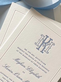 two folded wedding cards with the letter m on them, next to a blue ribbon