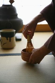 a person holding a whisk over a wooden bowl on top of a mat