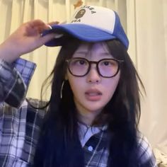 a girl wearing glasses and a hat is holding her hair in front of her face