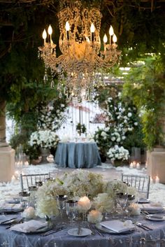 the table is set with white flowers, candles and place settings for an elegant dinner