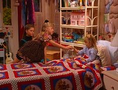 three children in a bedroom playing with a quilt on the bed and another child reaching for it