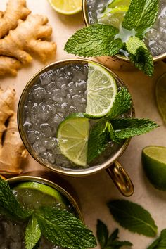 two glasses filled with ice and limes next to sliced ginger, mint and lemon