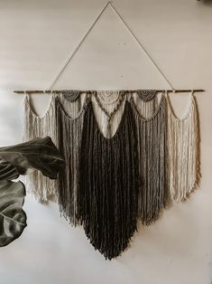 a wall hanging with fringes on it and a plant in the corner next to it