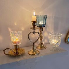 three candles are sitting on top of a table next to some glass bowls and vases