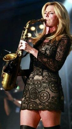 a woman in black dress holding a saxophone and wearing thigh high boots with lace on it