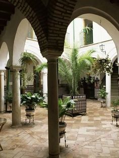 an indoor courtyard with potted plants and benches in the center, surrounded by arches