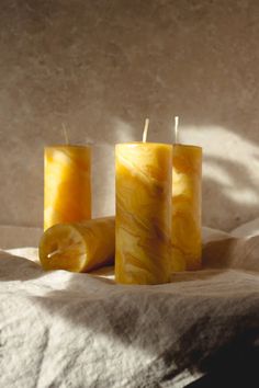 three yellow candles sitting on top of a bed next to each other with one candle in the middle