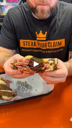 a man is holding a sandwich in his hands while sitting at a table with other food items