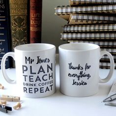 two coffee mugs sitting next to each other on top of a white table with books in the background