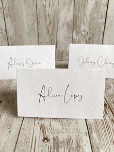 two white cards with black ink on them sitting next to each other in front of a wooden background