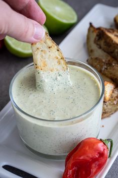 a person dipping a piece of bread into a bowl of ranch dressing with a red pepper on the side