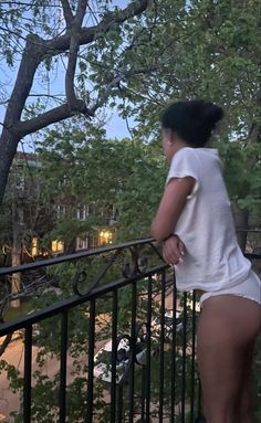 a woman in white shirt and shorts standing on railing next to trees