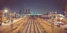 an empty train track in the middle of a city at night with tall buildings and lights