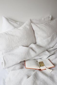 an open book laying on top of a bed with white sheets and pillowcases