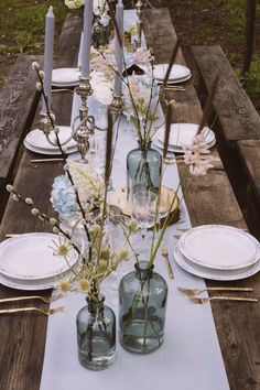 a long table with plates and vases on it is set for an outdoor dinner