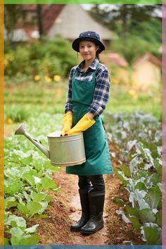 a woman in an apron and rubber boots is holding a watering can while standing in a garden