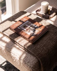 a book sitting on top of a table next to a cup and saucer in front of a window