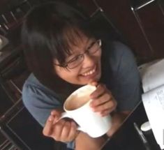 a woman sitting at a table drinking from a coffee cup and smiling for the camera