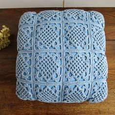 a blue crocheted pillow sitting on top of a wooden table next to a flower