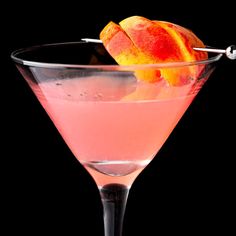 a pink martini with peaches in it and garnished with an orange peel