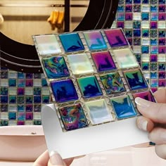 a person holding up a sticker in front of a bathroom wall with colorful tiles on it