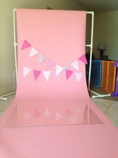 a pink backdrop with bunting flags and streamers on the top, in front of a tiled floor