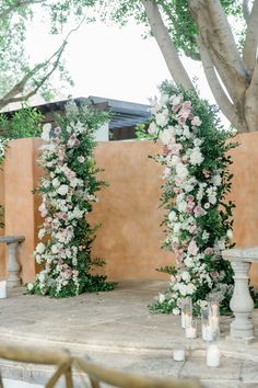 an outdoor wedding setup with flowers and candles on the table in front of a wall