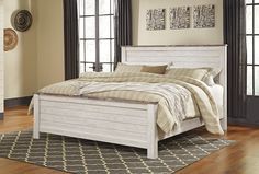 a white bed sitting on top of a wooden floor next to a window in a bedroom