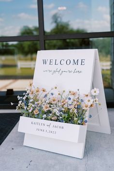 a welcome sign sitting on top of a table next to a flower pot filled with flowers