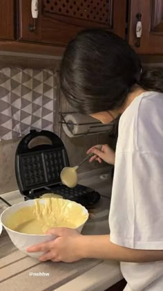 a woman in white shirt preparing food on top of a kitchen counter next to waffle iron