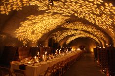 a long table is set up in the middle of a dimly lit room with many candles on it