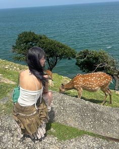 a woman sitting on top of a cliff next to a deer